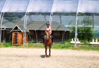 Person reitet ein braunes Pferd unter einer Überdachung im Feather Down Ecuries de Gapennes, Hauts-de-France, Frankreich.