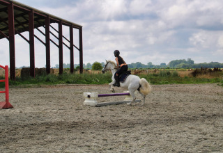 Jinete salta un obstáculo con caballo blanco en pista exterior de Feather Down Ecuries de Gapennes, Francia.