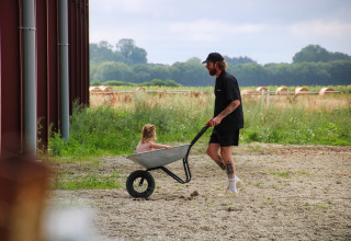 Een man duwt een kruiwagen met een klein kind bij Feather Down Ecuries de Gapennes vakantiepark in Frankrijk.