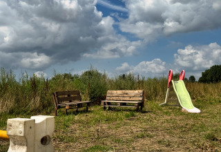 Bankjes en een glijbaan op een grasveld onder een dramatische lucht bij Feather Down Ecuries de Gapennes, Frankrijk.