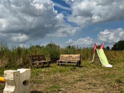Bankjes en een glijbaan op een grasveld onder een dramatische lucht bij Feather Down Ecuries de Gapennes, Frankrijk.