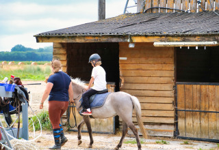 Barn rider på pony ledsaget af voksen foran en træstald ved Feather Down Ecuries de Gapennes, Hauts-de-France.