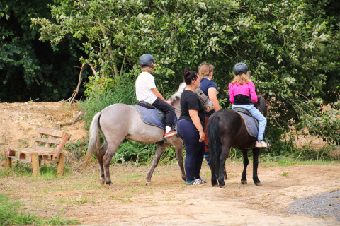 Kinderen en volwassenen met helmen rijden te paard in een bosrijk vakantiepark in Hauts-de-France, Frankrijk.