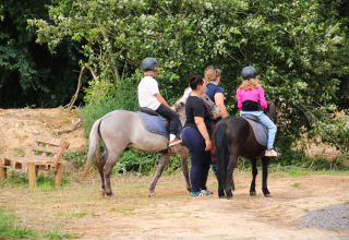 Kinderen en volwassenen met helmen rijden te paard in een bosrijk vakantiepark in Hauts-de-France, Frankrijk.
