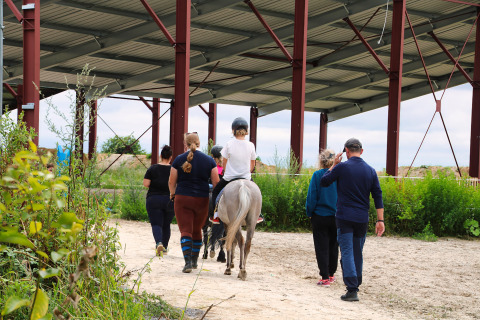 Groep begeleidt een kind op een paard onder een afdak bij Feather Down Ecuries de Gapennes, Hauts-de-France.