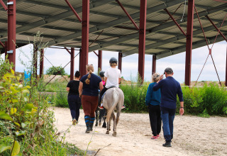 Groep begeleidt een kind op een paard onder een afdak bij Feather Down Ecuries de Gapennes, Hauts-de-France.