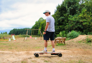 Man op skateboard in vakantiepark met schommels, glijbaan en bankje bij Feather Down Ecuries de Gapennes.