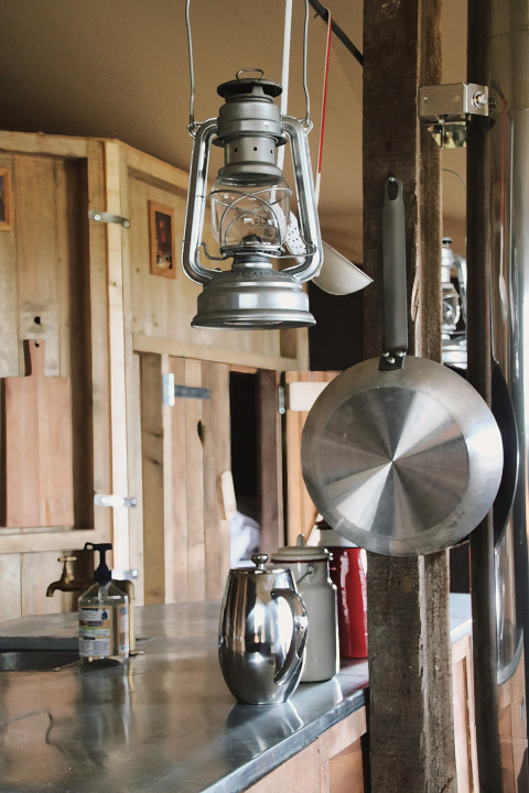 Landelijke keuken met hangende olielamp, pan en koffiepot op een metalen aanrechtblad.