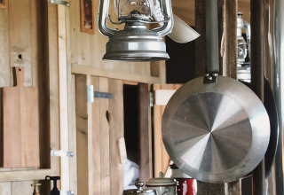 Rustikt køkkeninteriør med hængende petroleumslampe, stegepande og kaffekande på metalbord.