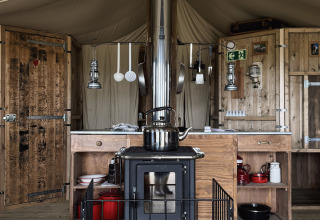 Rustic tent kitchen with a wood stove and wooden furnishings at Feather Down Ecuries de Gapennes, France.