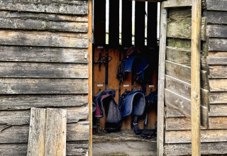 Een oude houten schuur met open deur toont zadels bij Feather Down Ecuries de Gapennes in Frankrijk.