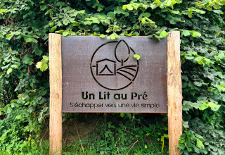 Holzschild mit Aufschrift 'Un Lit au Pré' bei Feather Down Ecuries de Gapennes, umgeben von Laub.
