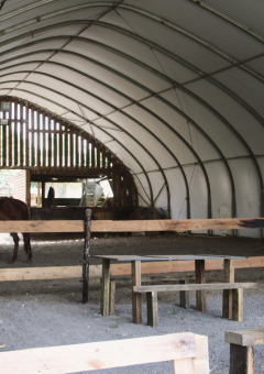 Interieur van een schuur bij Feather Down Ecuries de Gapennes met paarden, tafels en banken in Frankrijk.