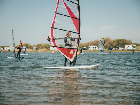 Windsurfers genieten van een zonnige dag op het water nabij Ouddorp, met campers op de achtergrond.