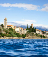 Coastal view with historic buildings and a glamping area at a holiday park, surrounded by trees and blue sea.