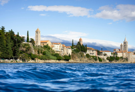 Kustzicht met historische gebouwen en glampingzone in vakantiepark, omgeven door bomen en blauwe zee.