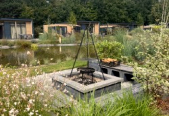 Udendørs bålplads med grill ved Batenburgh Deluxe-lodgen i Veluwepark de Bosgraaf, Holland, med hytter og natur.