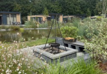 Focolare e barbecue all’aperto vicino al Batenburgh Deluxe lodge nel Veluwepark de Bosgraaf, Paesi Bassi, circondato dal verde.