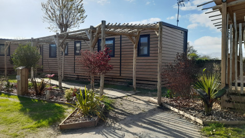 Billede af en Stacaravan Premium mobilhome med træpergola og velplejet have under en blå himmel.