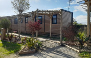 Mobil-home Stacaravan Premium avec pergola en bois et jardin paysager sous un ciel ensoleillé.