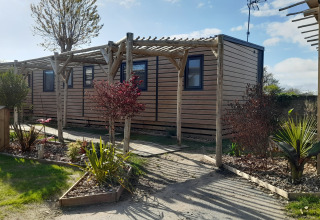 Billede af en Stacaravan Premium mobilhome med træpergola og velplejet have under en blå himmel.