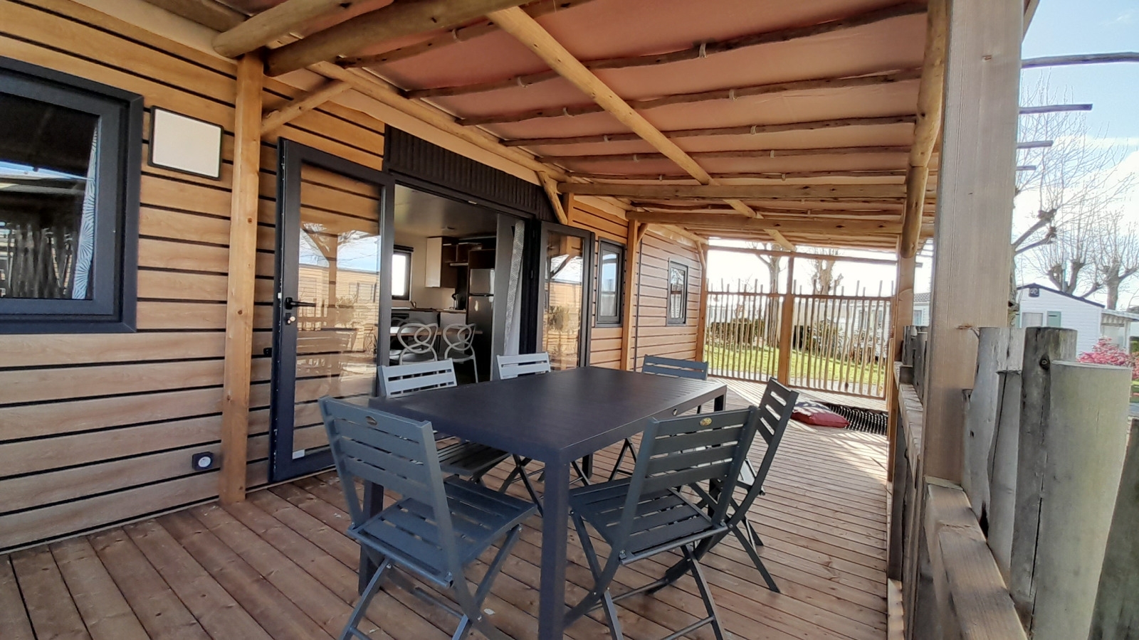 Overdekt houten terras met tafel en stoelen bij Stacaravan Premium, Flower Camping Le Pré des Sables, Frankrijk.