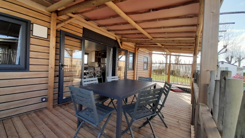 Terraza cubierta de madera con mesa y sillas en Stacaravan Premium, Flower Camping Le Pré des Sables, Francia.