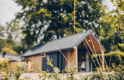 A photo of the Tiny Loft tiny house with a hot tub at Veluwepark de Bosgraaf in the Netherlands, surrounded by greenery.