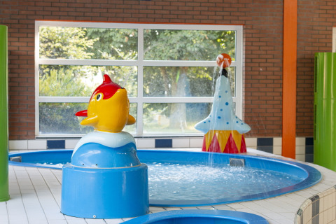 Indoor children’s pool with colorful water play structures, including a yellow fish, at Safarilodge Impala, IJsselhof.