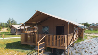 View of a Safarilodge Gazelle safari tent with a wooden deck on a grassy campsite under a clear sky.