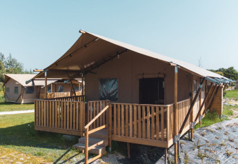 Vista di una tenda safari Safarilodge Gazelle con veranda in legno in un campeggio erboso sotto cielo sereno.