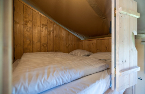 Cozy sleeping area with wooden walls at Safarilodge Impala, Vakantiepark IJsselhof, Netherlands, with bedding.