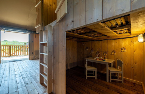 Intérieur d’un lodge safari avec mobilier en bois, coin enfants et terrasse, au Vakantiepark IJsselhof.