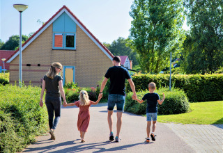 Eine vierköpfige Familie spaziert Hand in Hand vor einem Haus in einer grünen Siedlung in den Niederlanden.