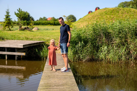 Father and daughter standing on a wooden pier by the water at Safarilodge Impala, Vakantiepark IJsselhof.