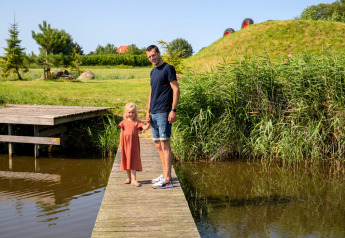 Father and daughter standing on a wooden pier by the water at Safarilodge Impala, Vakantiepark IJsselhof.