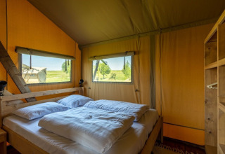 Chambre du Safarilodge Impala au Vakantiepark IJsselhof, Pays-Bas, avec lit double et fenêtres sur la nature.