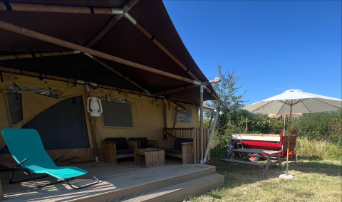 Tienda safari glamping con terraza de madera y sombrilla en Per Amore del Vino, Italia, bajo un cielo azul.