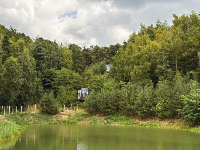 Cabaña acuática y jacuzzi en Cosy Cabins, bosque de Limburgo, Bélgica, con vista a un estanque y árboles.