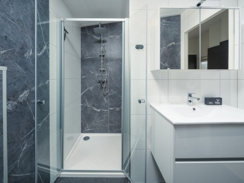 Moderne badkamer met glazen douche, wit wastafelmeubel en spiegels in Loevestein Deluxe, Veluwepark de Bosgraaf.