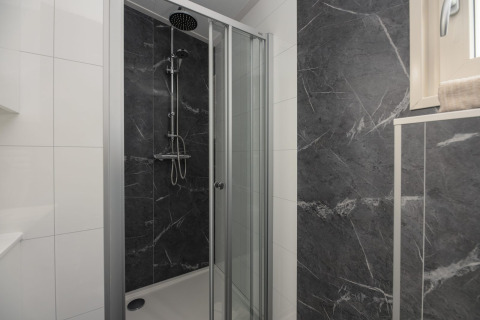 Moderne douchecabine met glazen deur en donkere marmerlook tegels in de badkamer van Loevestein Deluxe Lodge.