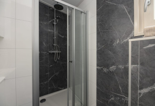 Moderne douchecabine met glazen deur en donkere marmerlook tegels in de badkamer van Loevestein Deluxe Lodge.