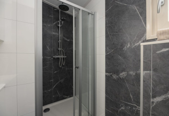 Moderna cabina de ducha con puerta de cristal y azulejos oscuros tipo mármol en Loevestein Deluxe Lodge.