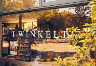Vitrine du magasin TWINKELT reflétant des arbres, prise à Loevestein Deluxe aux Pays-Bas.
