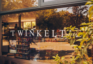 Winkelraam met TWINKELT erop en weerspiegeling van bomen, gemaakt bij Loevestein Deluxe in Nederland.