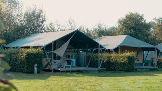 Safari cottage safari-telt med overdækket terrasse og grønne omgivelser under solrigt vejr.