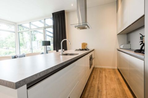 Modern kitchen in Module II lodge at Landgoed de Scheleberg, Netherlands, featuring wood flooring and windows.