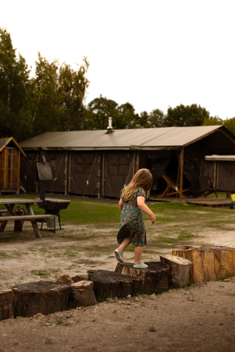 Een kind loopt over boomstammen bij Feather Down Het Keelven, een vakantiepark in Noord-Brabant, Nederland.
