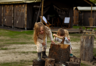 Deux enfants jouent près de rondins devant une tente au parc de vacances Feather Down Het Keelven, Brabant septentrional, Pays-Bas.