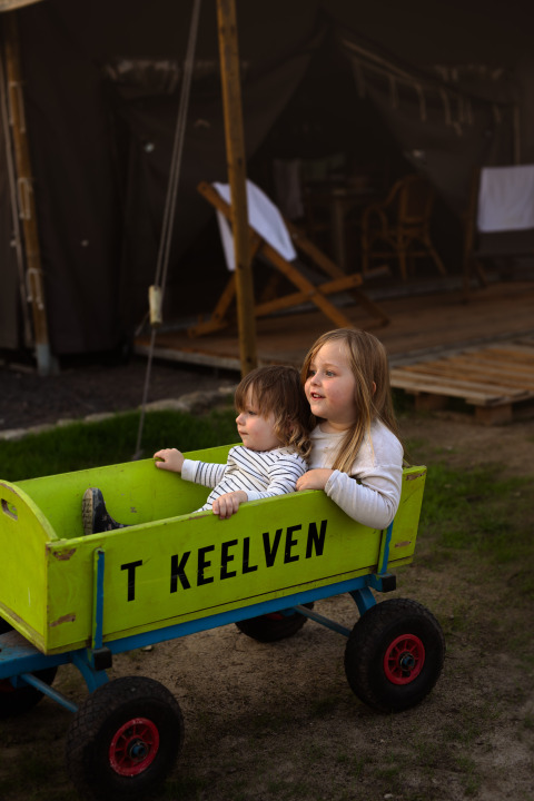 Dos niños juegan en un carro verde con 'T KEELVEN' en Feather Down Het Keelven, Brabante Septentrional, Países Bajos.